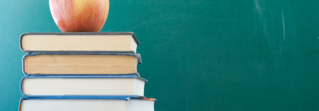 Ein roter Apfel liegt auf einem Stapel Bücher vor einer grünen Tafel.