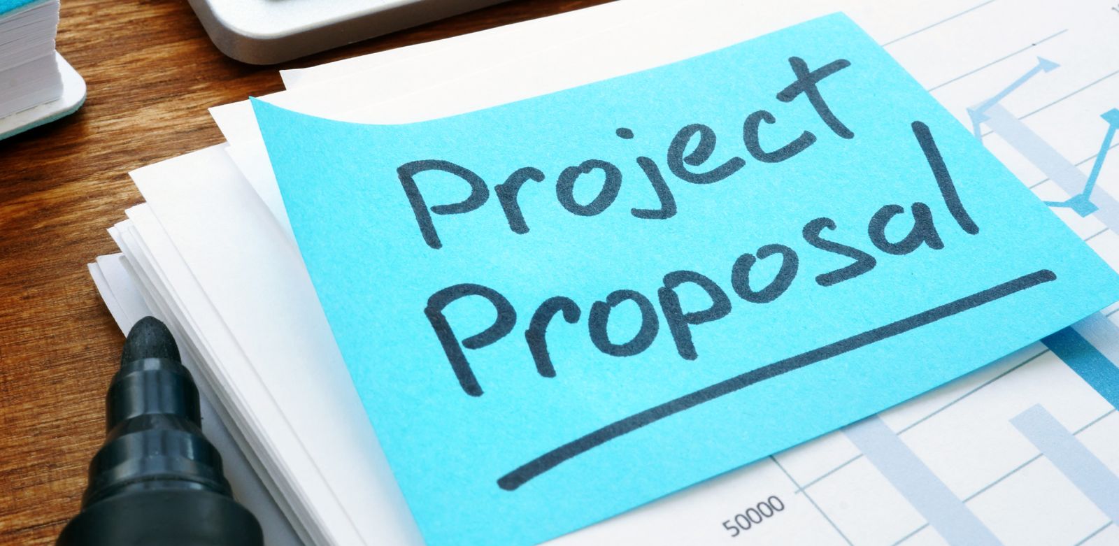 Ein Stapel Papier mit einer blauen Haftnotiz, auf der "Project Proposal" steht, daneben liegt ein schwarzer Filzstift.