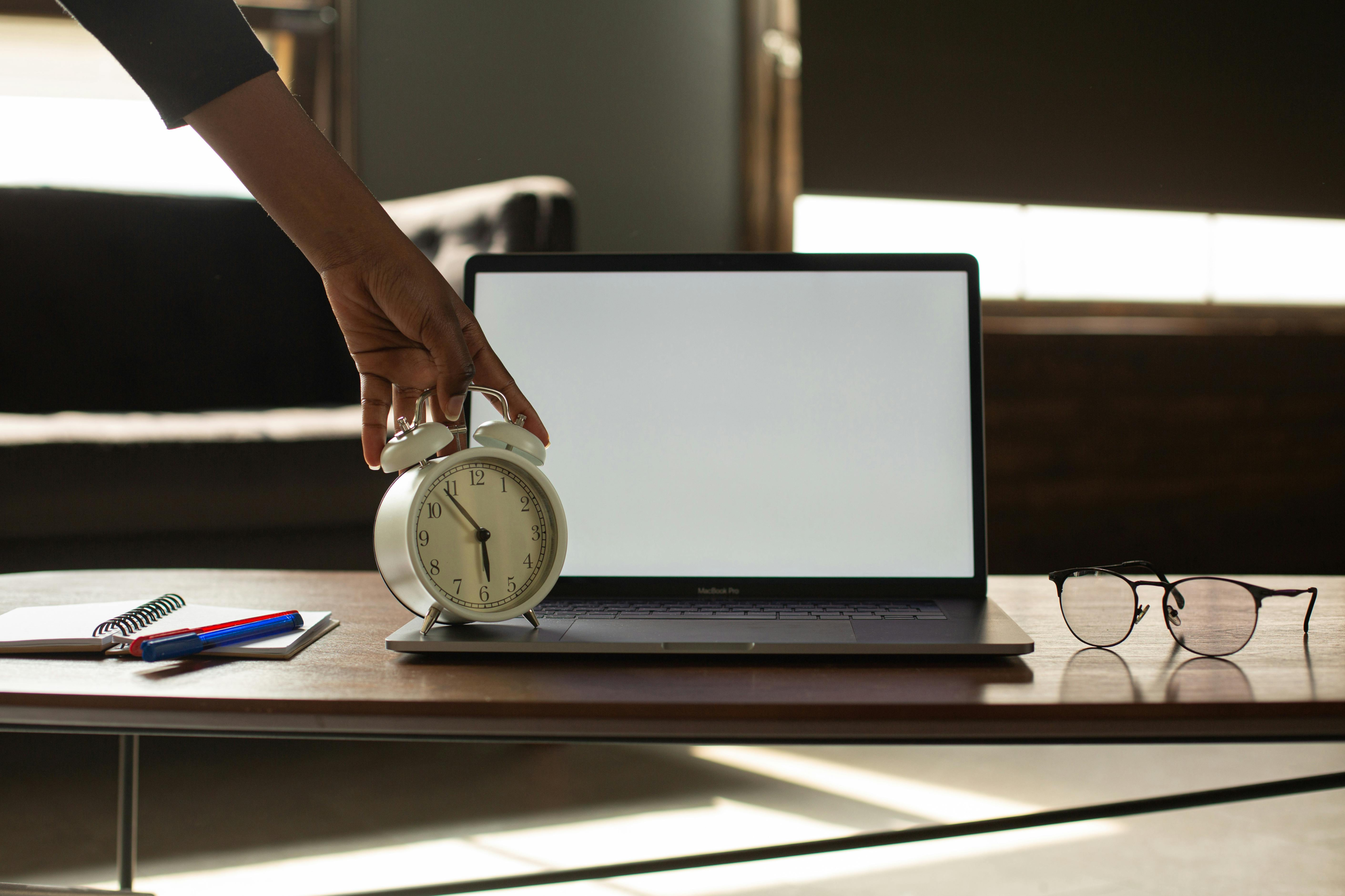 Hand stellt Wecker aus vor Laptop