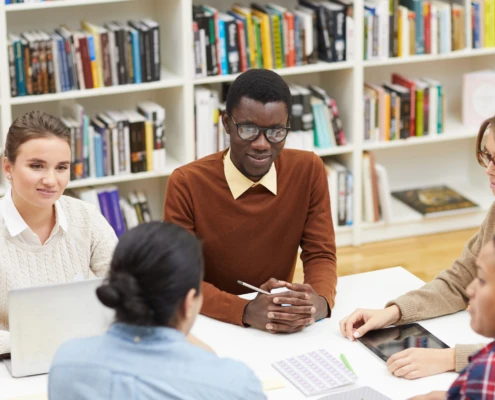 Gruppe von fünf Personen sitzt an einem Tisch in einer Bibliothek und arbeitet gemeinsam an einem Projekt.